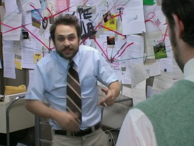 Charlie explains his mailroom conspiracy to Mac in front of a wall covered with papers and red lines.