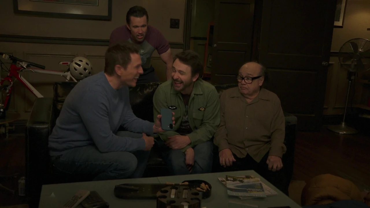 Dennis, Charlie, Frank and Mac crowd around a phone during their failed prank call to Dee.